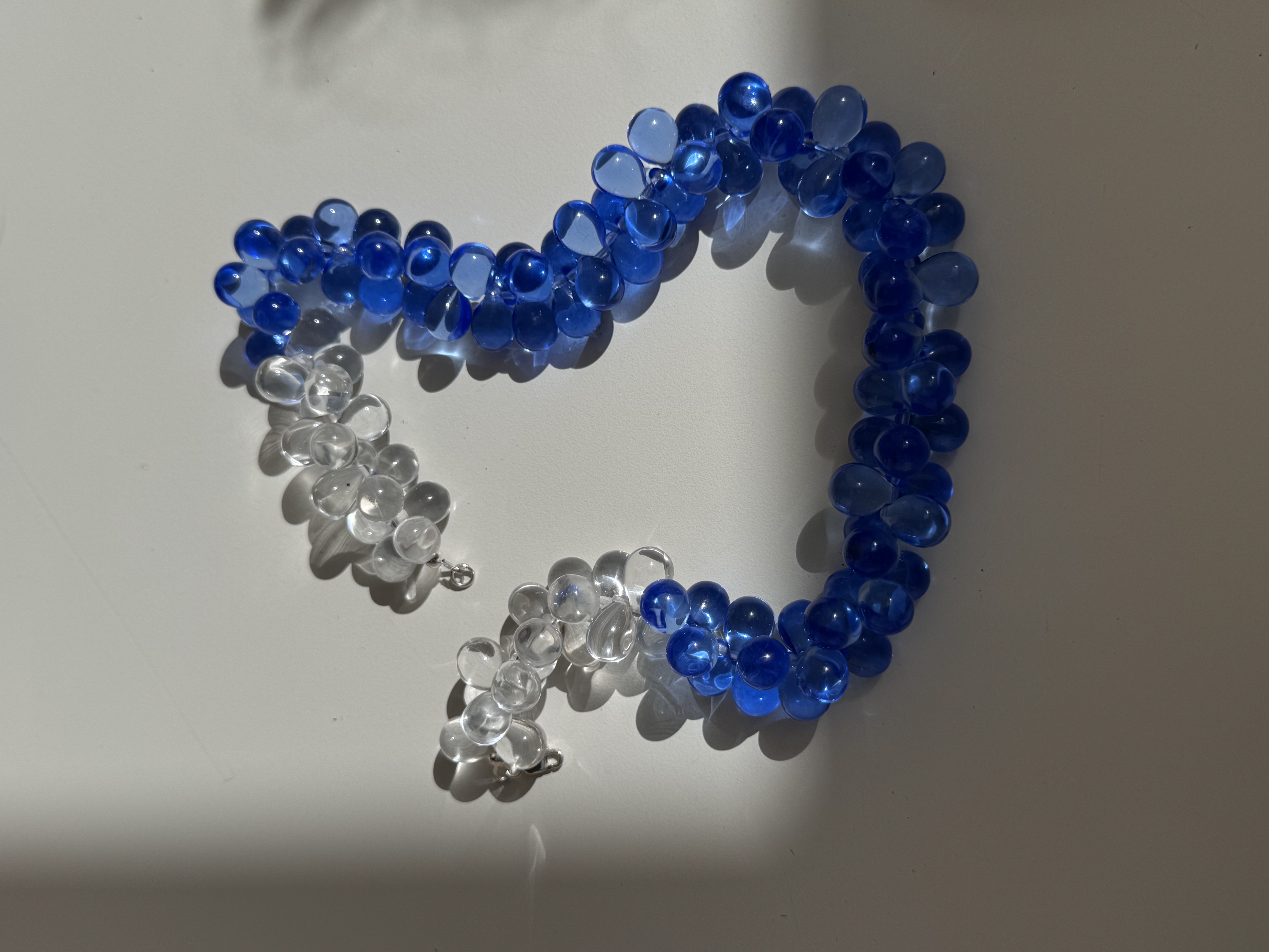 Choker-style necklace made of translucent blue round beads in ocean-inspired shades. The shape of the beads creates a layered effect while remaining a single strand.
Glass beads
Sterling silver hardware
43 cm length
Handcrafted in Berlin