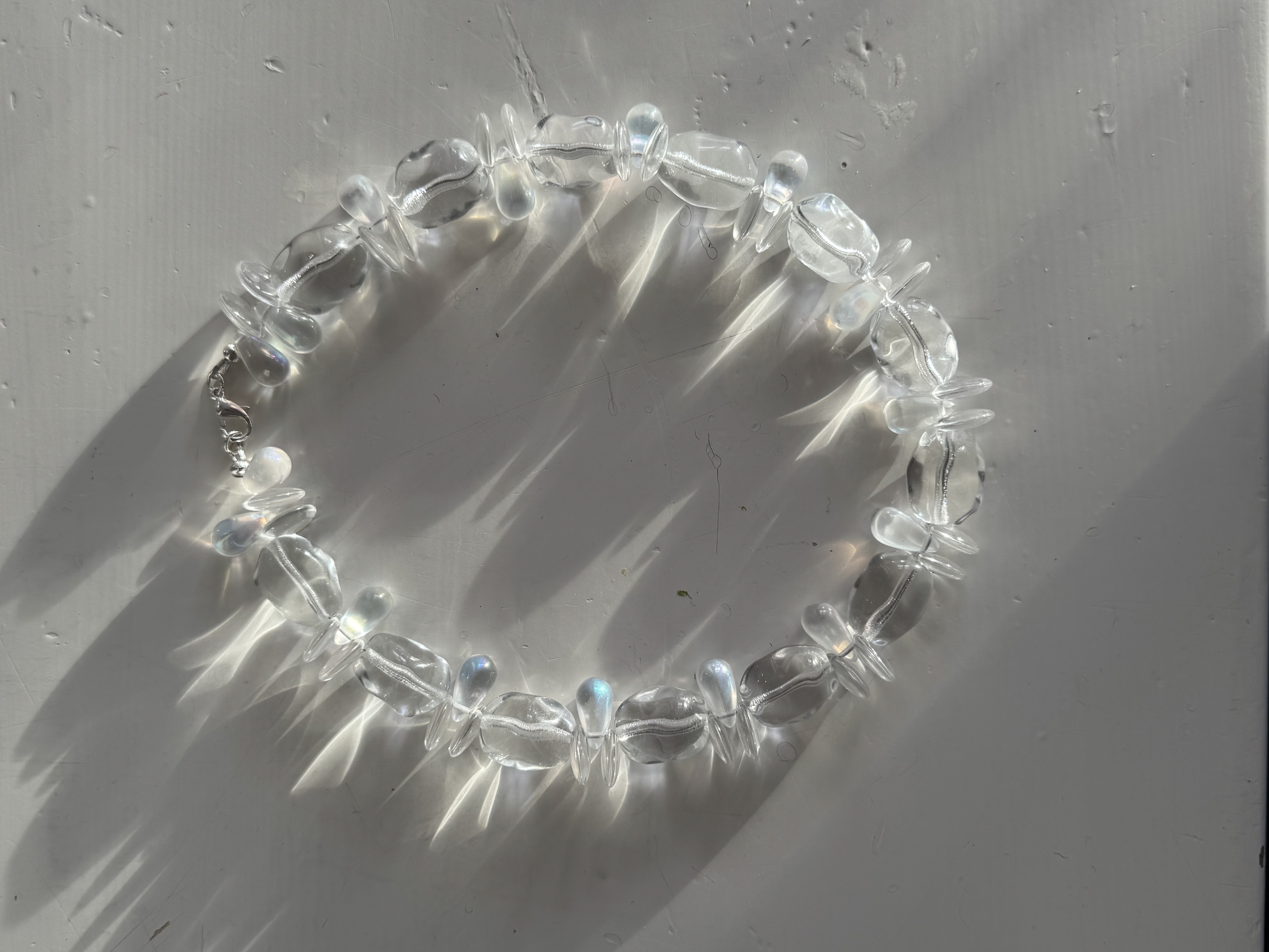 A sculptural necklace of clear glass beads with iridescent drops. Light, fluid, and luminous — inspired by reflections of water and movement.

Glass beads 
Sterling silver hardware

42 cm length

Handcrafted in Berlin